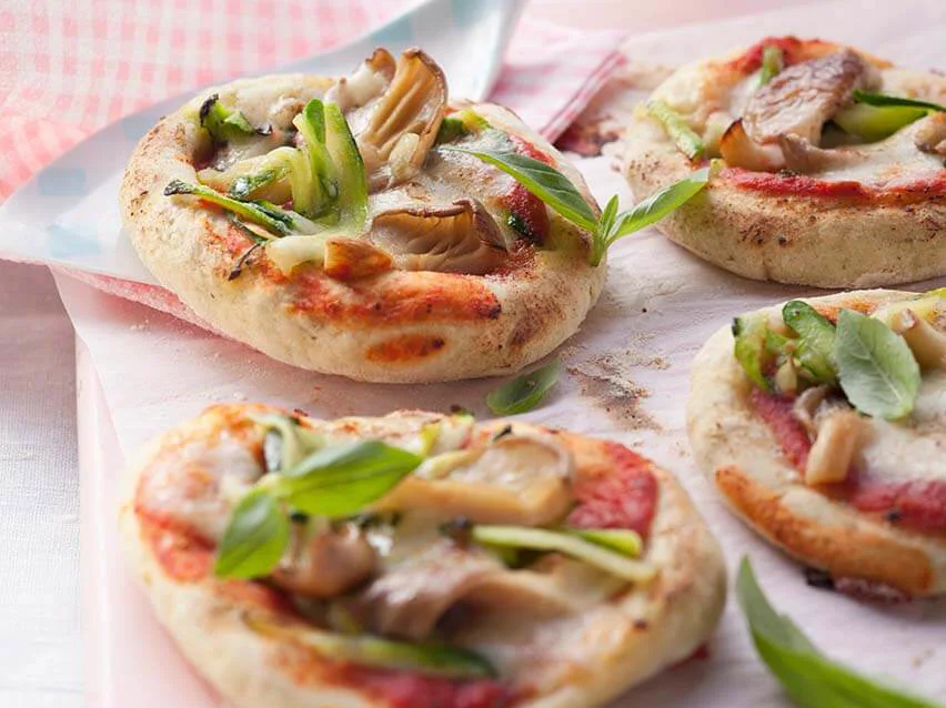 Mehrere kleine Pizzen mit Zucchinischeiben und Austernpilzen