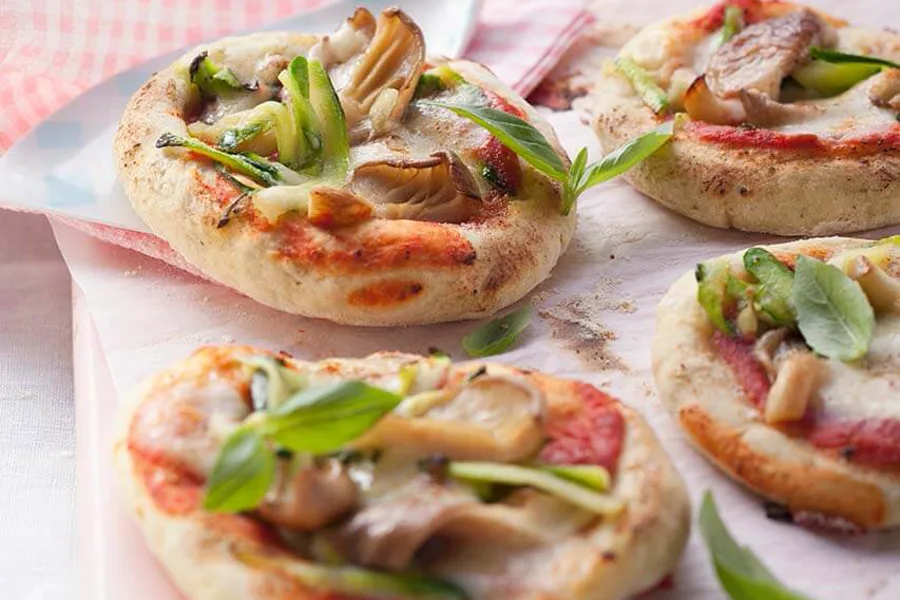 Mehrere kleine Pizzen mit Zucchinischeiben und Austernpilzen